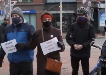 People wearing face masks hold signs that say People Before Profit and Rent Control Now.