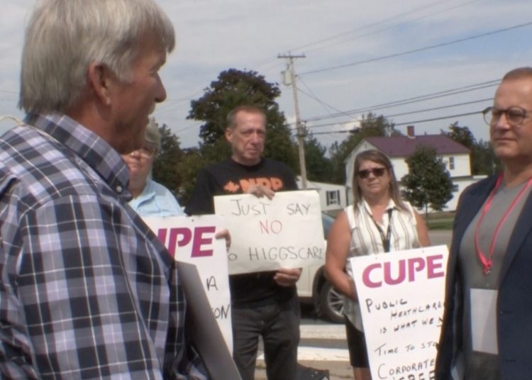 Several people holding placards listen while the union president addresses a member of parliament.
