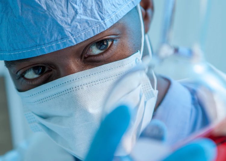 A man in scrubs investigates a vial of liquid.