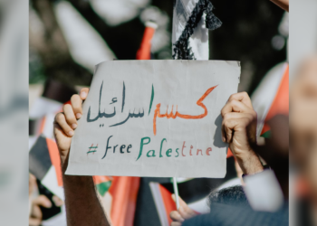 Someone holds a sign with Arabic writing on it. Underneath it is "Free Palestine."