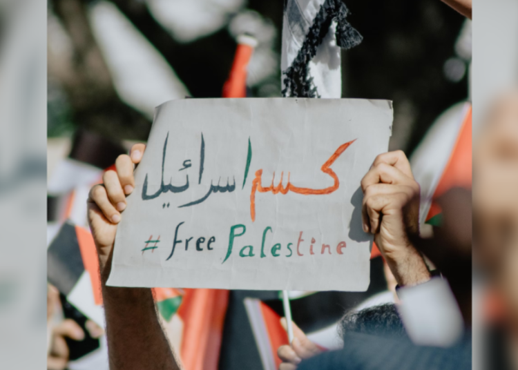 Someone holds a sign with Arabic writing on it. Underneath it is "Free Palestine."