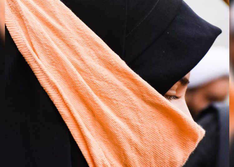 A woman wearing a black head covering and an orange bandana.