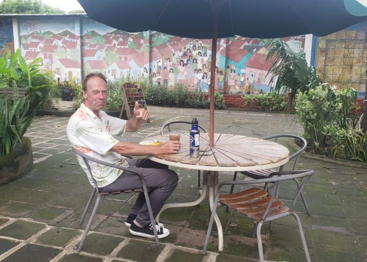 Dirk Groenenberg at a patio table at Casa Benjamin Linder, Managua, Nicaragua, giving a thumbs-up with a mural in the background.