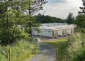 Rows of large white battery storage containers in a fenced facility surrounded by trees and greenery.