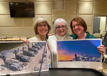 hree members of the Stop the Tantramar Gas Plant group stand together smiling and holding large posters with images of gas plants; left to right are Juliette Bulmer, Terry Jones, and Kristen LeBlanc.