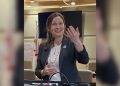Tantramar MLA Megan Mitton standing and speaking to the public, wearing a dark grey blazer and gesturing with her hand.
