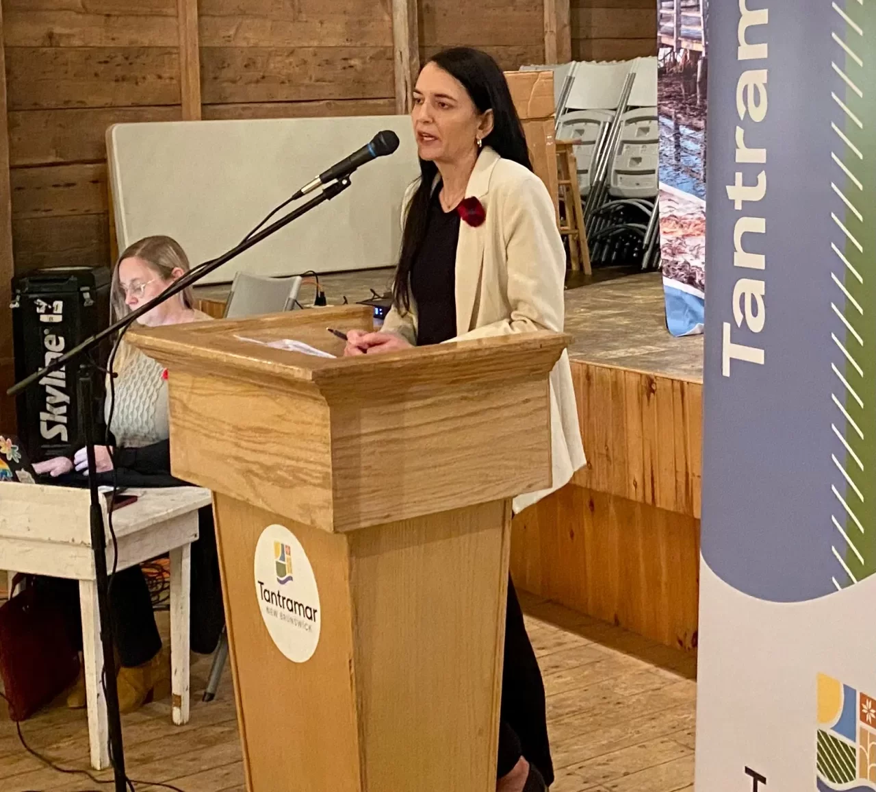 Tantramar CAO Jennifer Borne, wearing a light jacket and black top, speaks from behind a wooden podium at the community meeting.