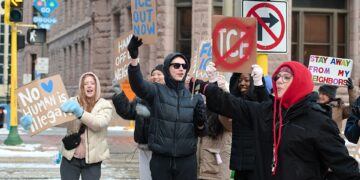 Des manifestants brandissent des pancartes avec les messages « No human is illegal », « ICE out now » et « Stay away from my neighbors » lors d'un rassemblement contre l'ICE au centre-ville de Minneapolis.