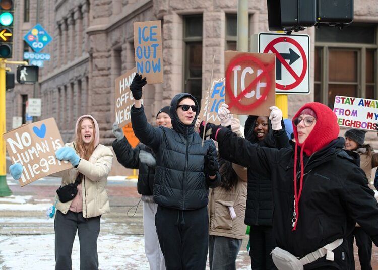 Des manifestants brandissent des pancartes avec les messages « No human is illegal », « ICE out now » et « Stay away from my neighbors » lors d'un rassemblement contre l'ICE au centre-ville de Minneapolis.