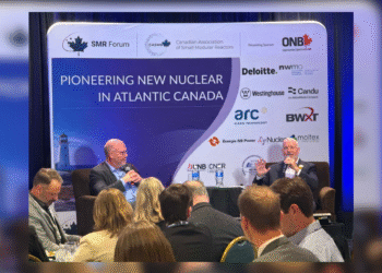 Two men sit on stage holding microphones during a panel discussion, in front of a backdrop reading 'Pioneering New Nuclear in Atlantic Canada' with sponsor logos including Westinghouse, NB Power, NWMO, and Candu. An audience is seated in the foreground.