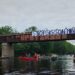 Paddlers pass beneath a bridge bearing a "Stop Sisson Mine" banner and a Wolastoq flag on the Nashwaak River.